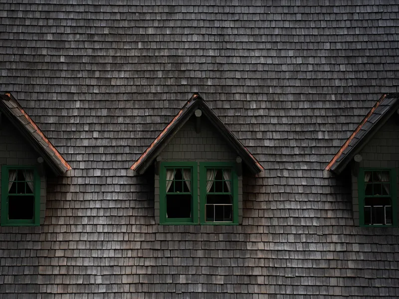 Weathered wood shake roof with three green-trimmed dormer windows